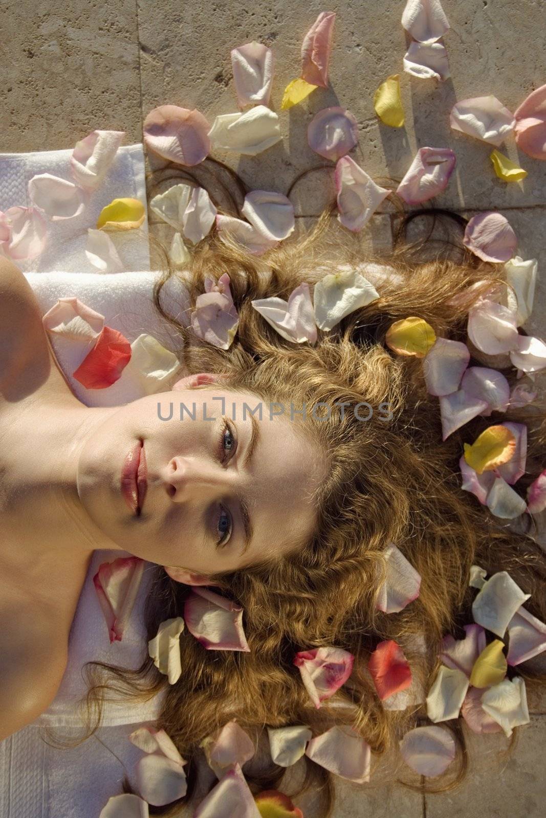 Above view of bare Caucasian mid-adult woman lying down with hair spread out on rose petals.