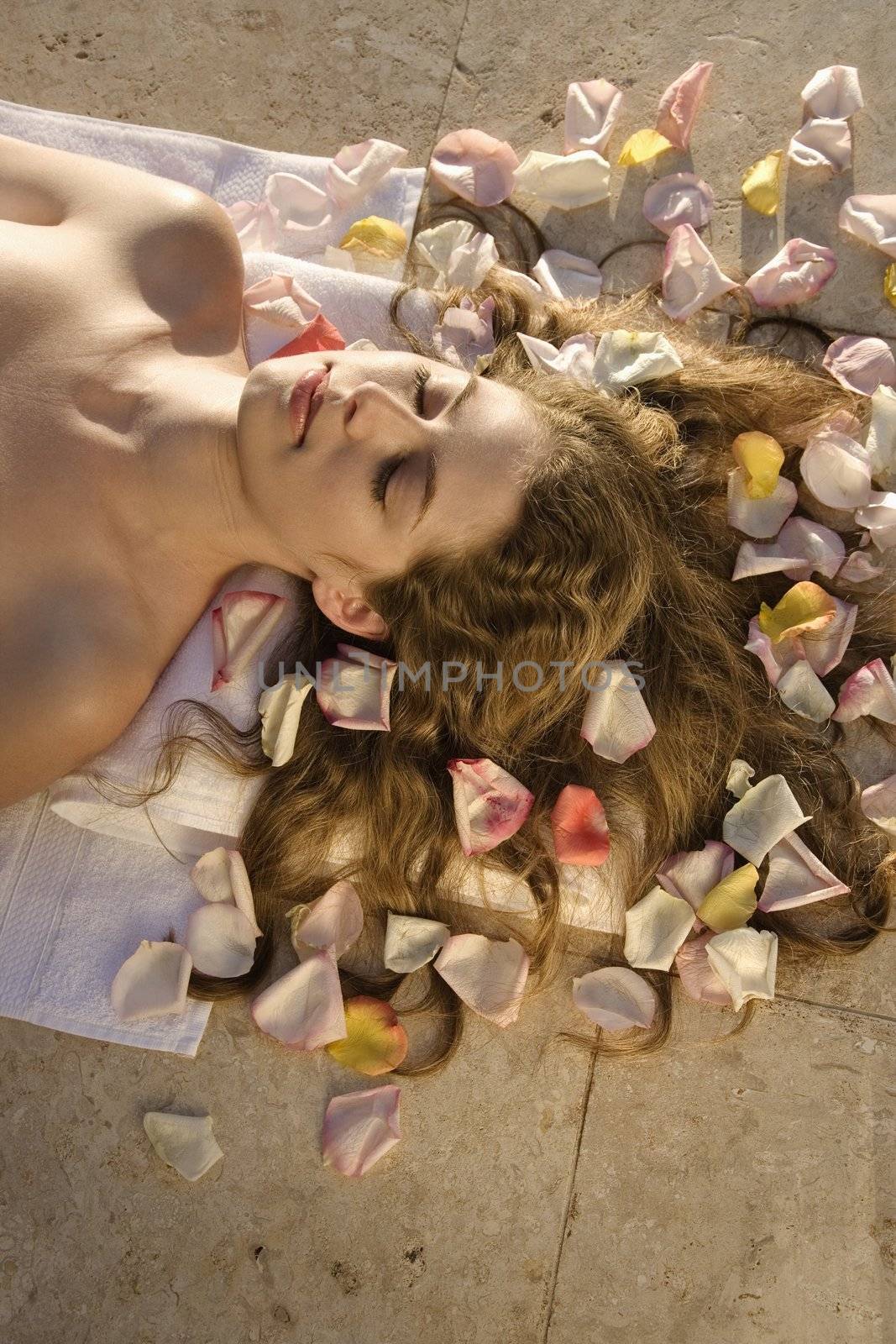 Above view of bare Caucasian mid-adult woman lying down with hair spread out on rose petals.