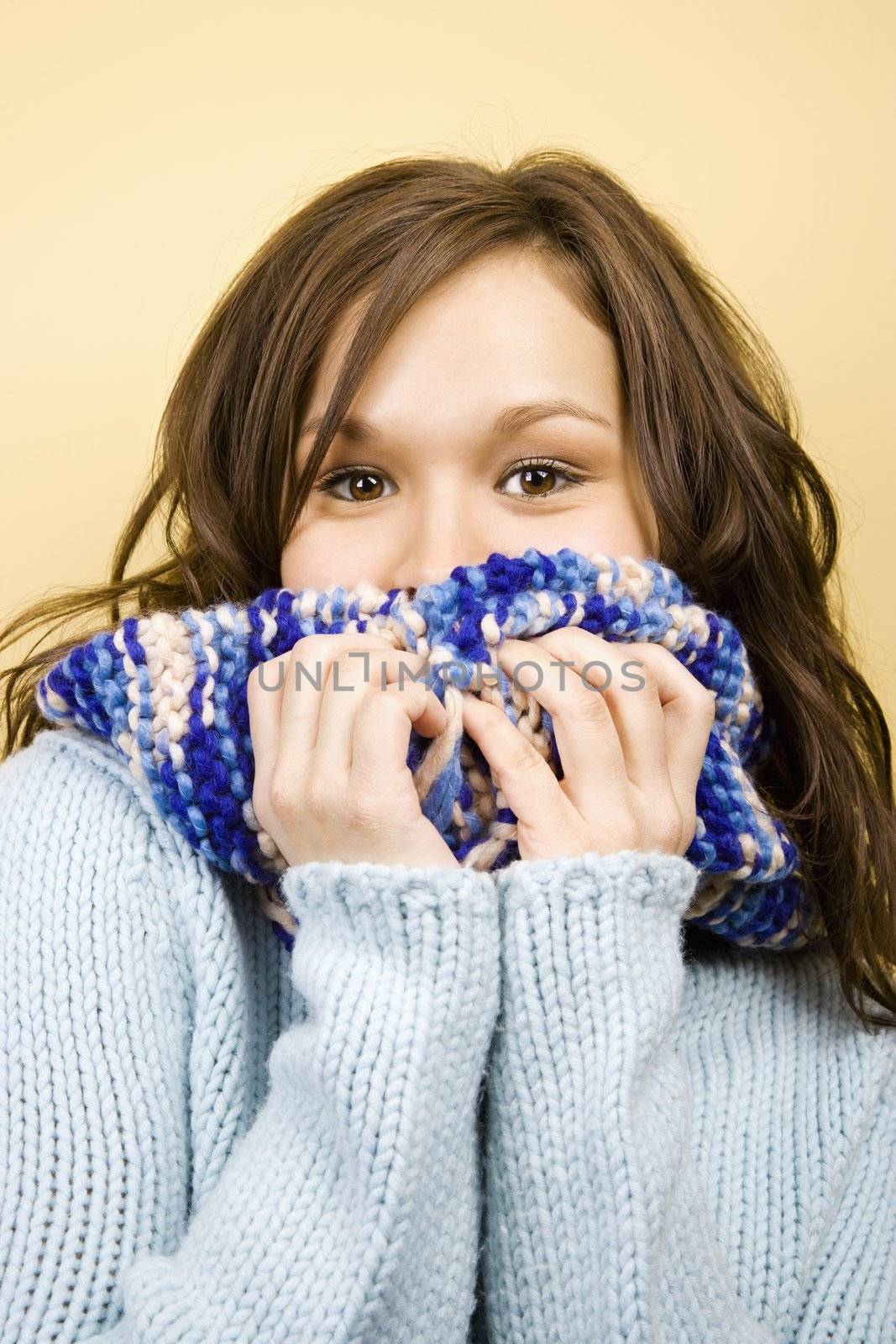 Young adult Caucasian woman covering mouth with scarf and looking at viewer.