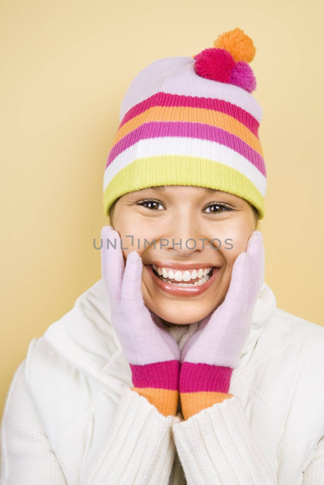 Young adult Caucasian woman wearing winter hat and gloves with hands to face smiling at viewer.