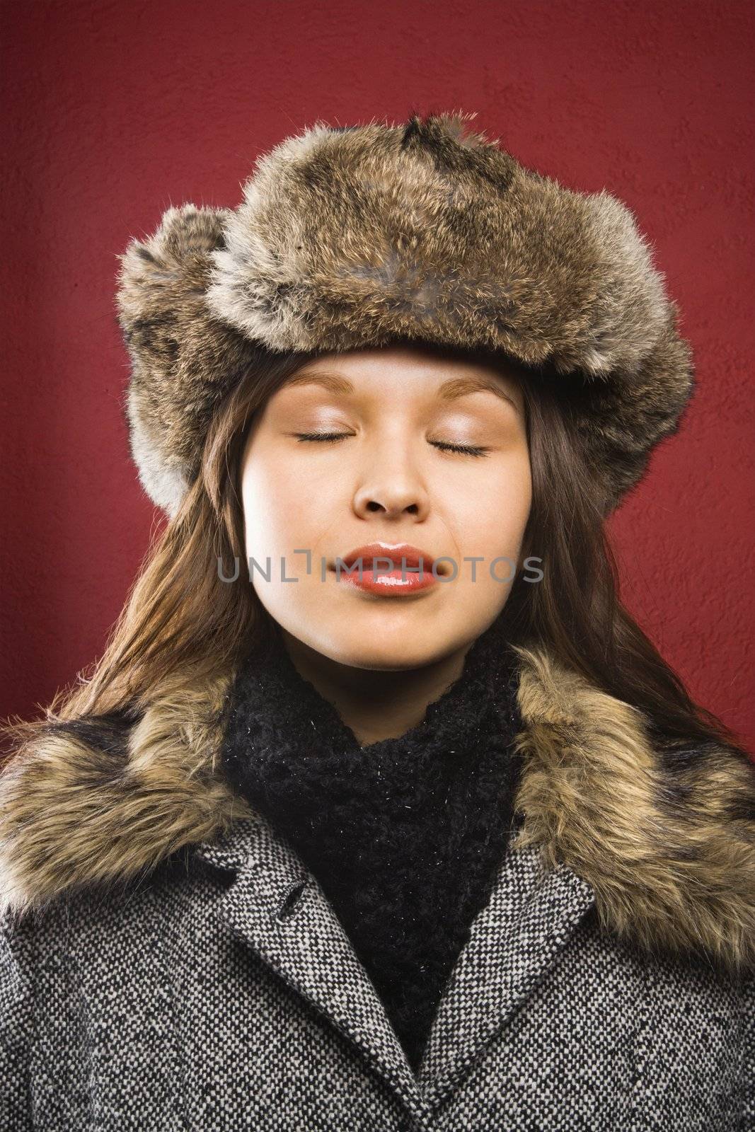 Young adult Caucasian woman wearing fur hat with eyes closed.