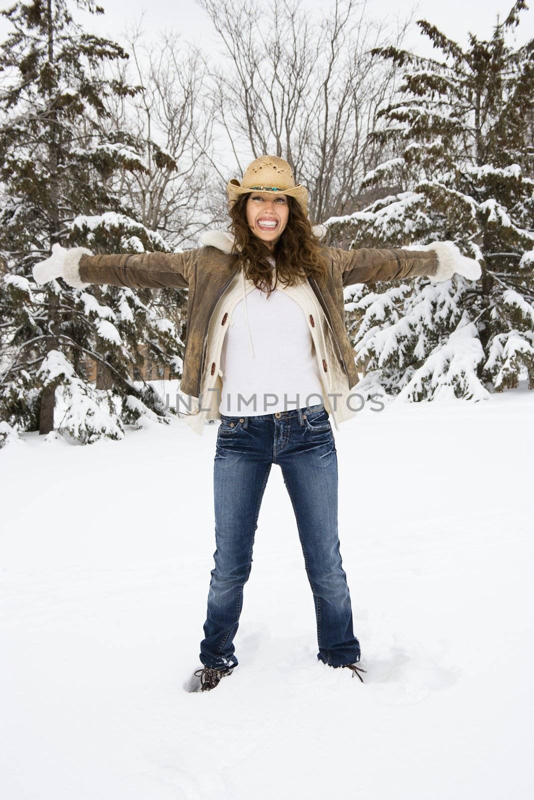 Caucasian young adult female standing with arms outstretched in snow wearing straw cowboy hat.