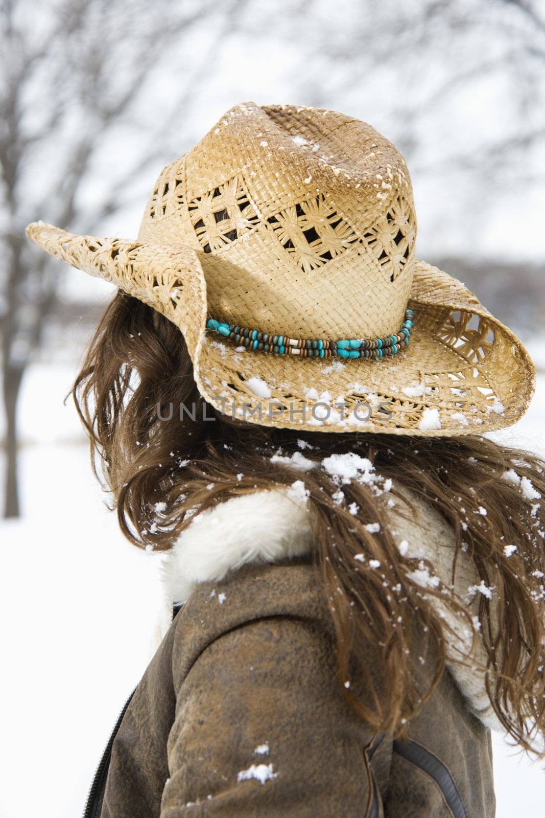 Back view of brunette woman with long hair wearing straw cowboy hat outdoors.