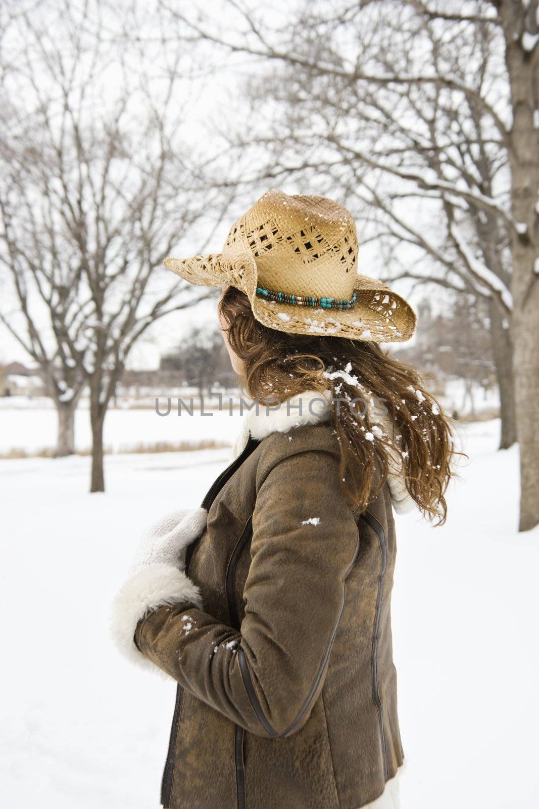 Back view of brunette woman with long hair wearing straw cowboy hat outdoors in the snow.