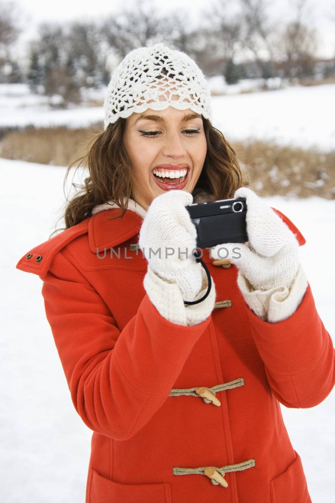 Smiling Caucasian young adult female in winter clothing using digital camera outdoors.