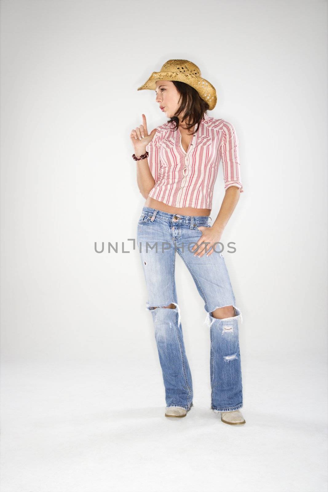 Young adult Caucasian woman wearing cowboy hat pointing finger upwards like gun and blowing away imaginary smoke.