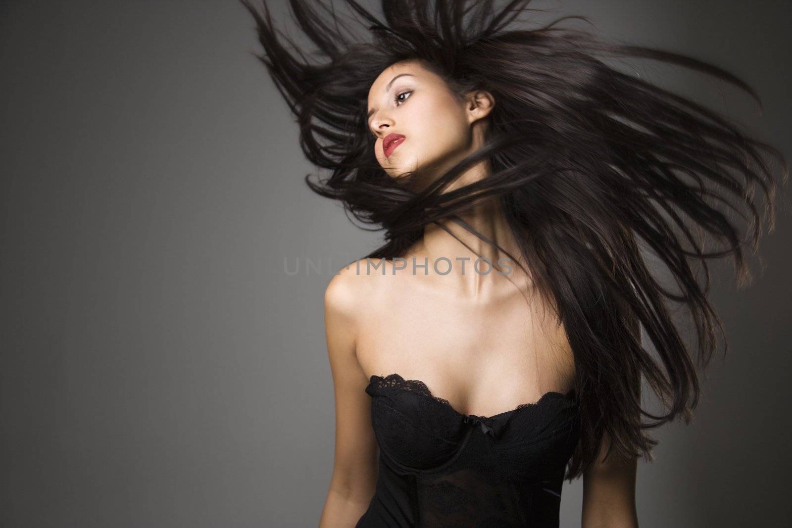 Portrait of pretty young woman flinging long black hair into air.