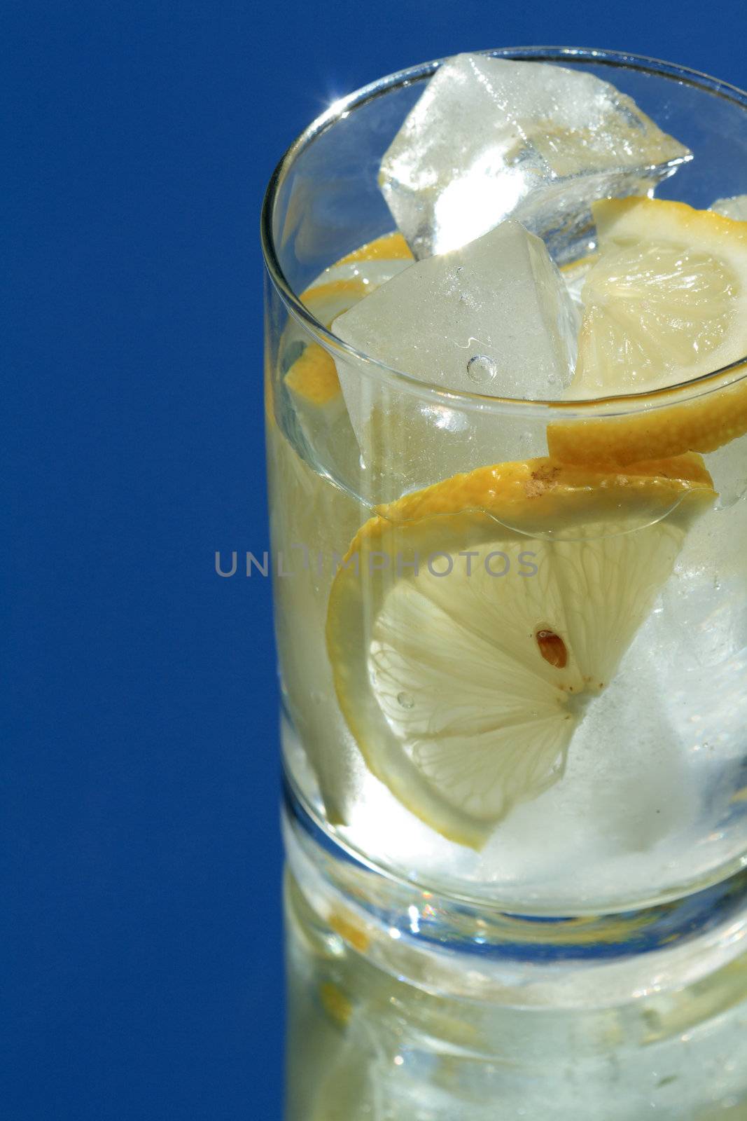 Glass of water with lemon and ice cubes on blue background