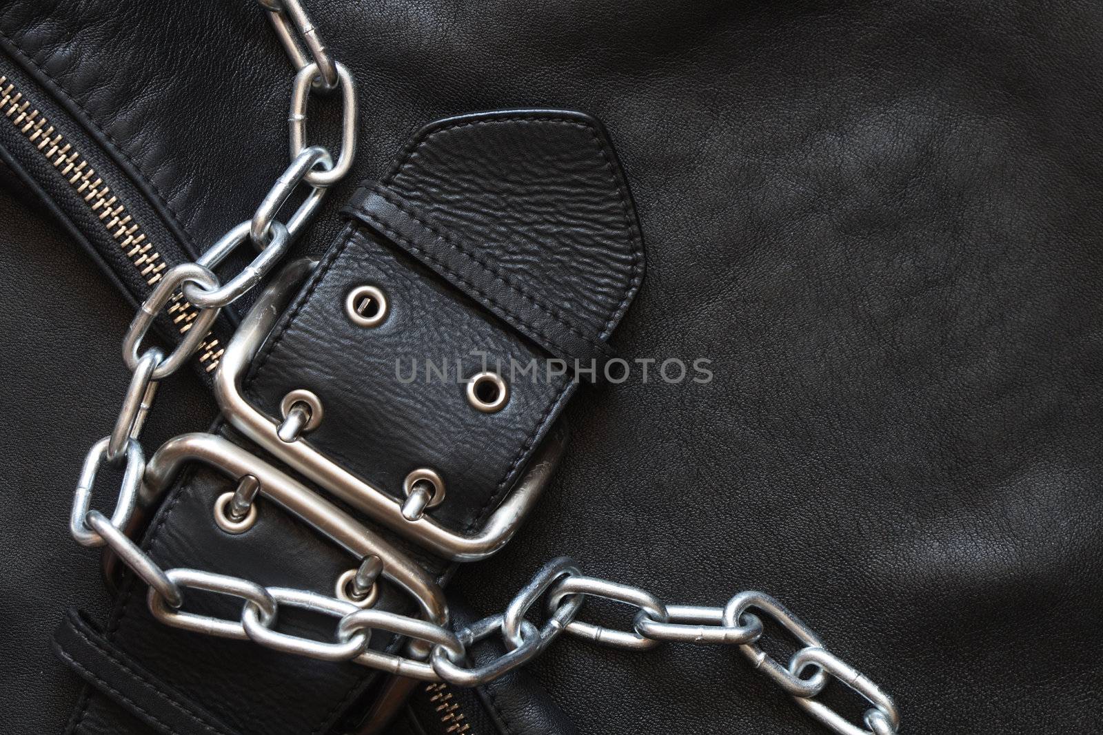 Metal chain lying on black leather background with clasp and zipper