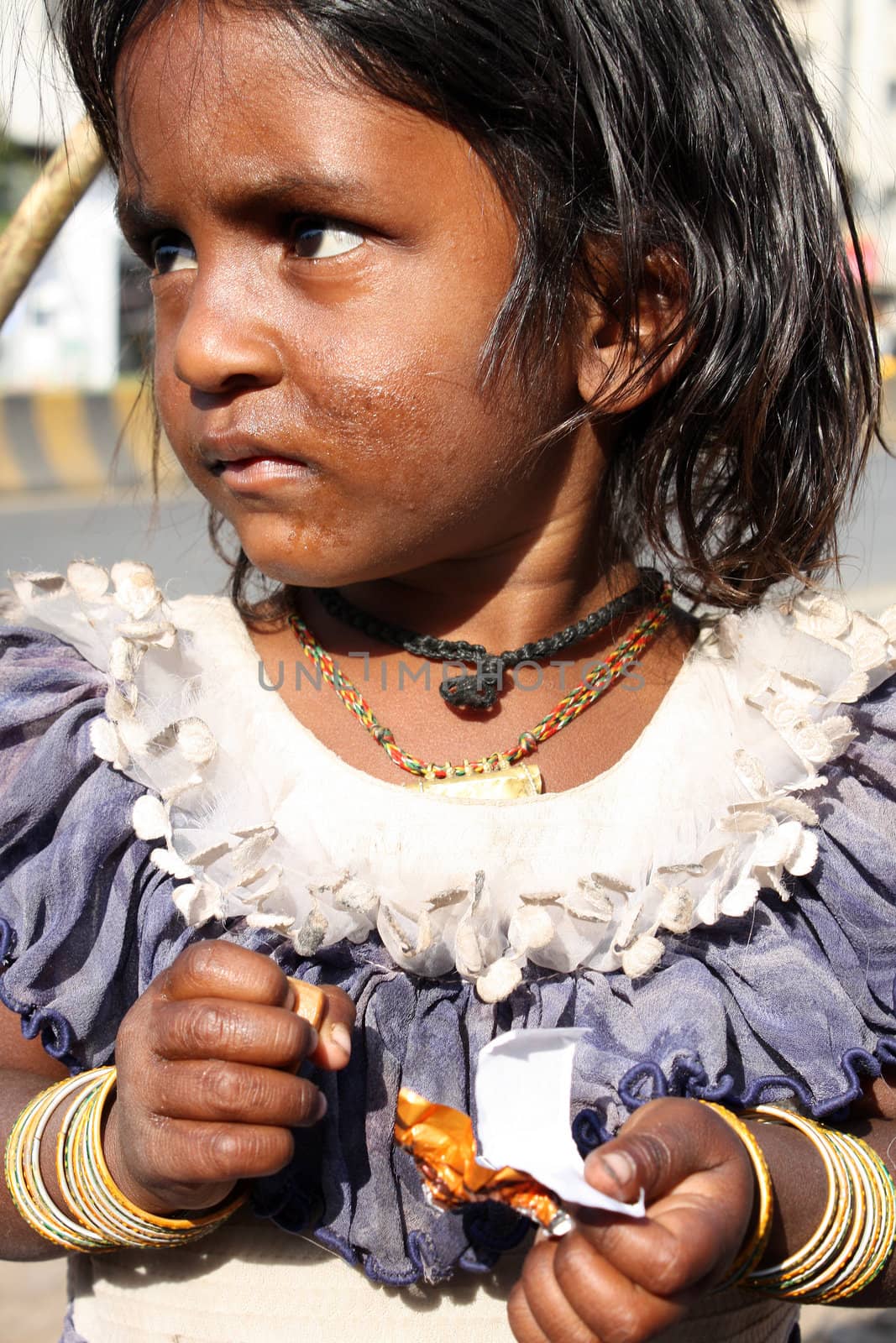 A portrait of a sad Indian beggar girl with an empty chocolate wrapper, standing on the streetside.