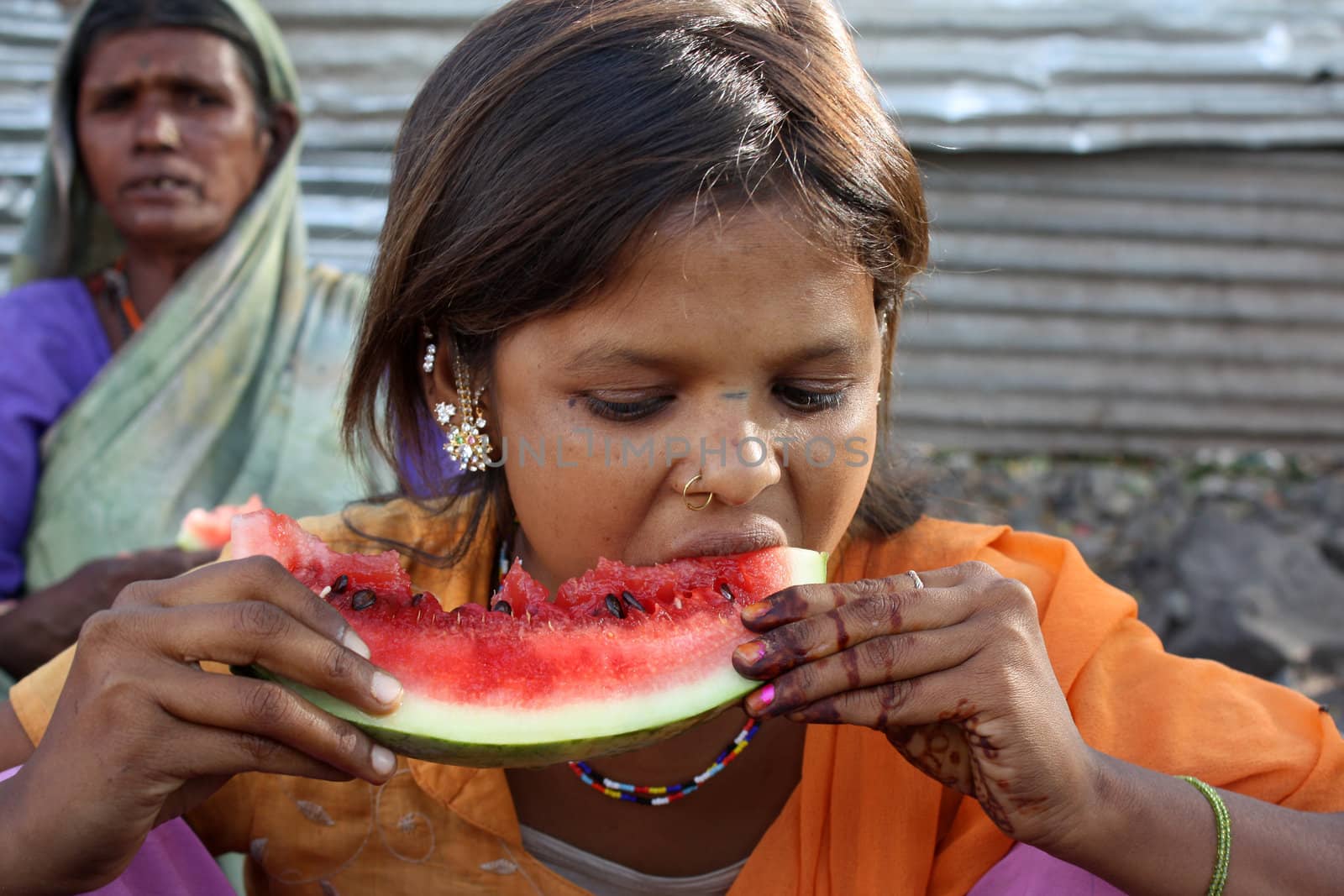 A poor beggar teenage girl in the Indian slums eating a fresh watermelon.