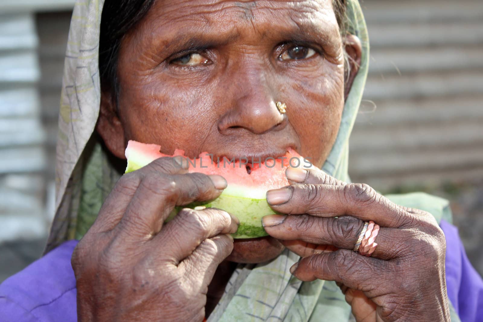 A very poor & hungry Indian woman eating a watermelon. Focus is on the hand and melon.