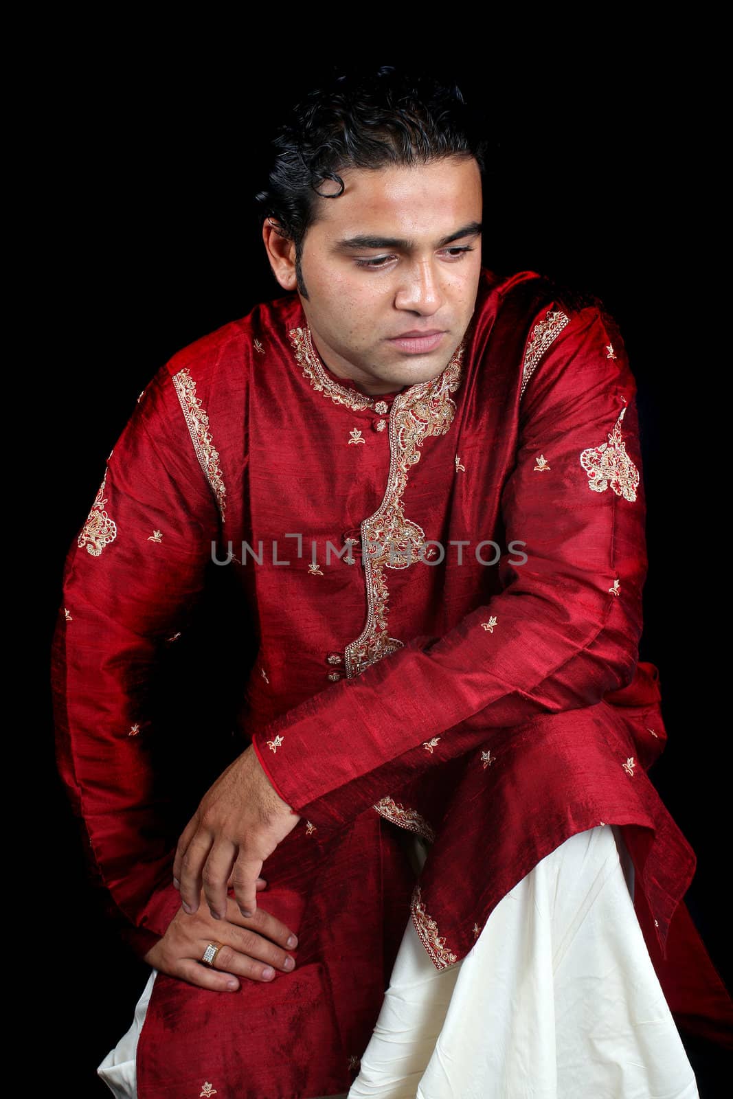 A daydreaming Indian man in a traditional attire, on black studio background.