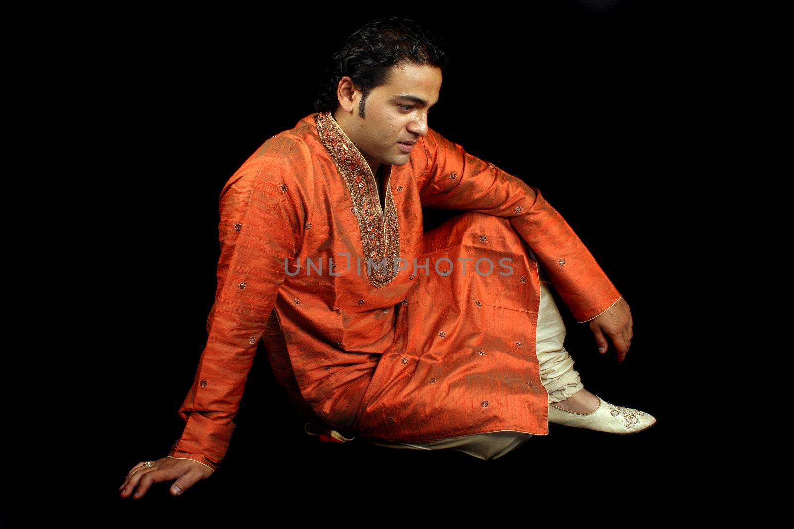 A handsome Indian man in a traditional royal attire in a sad mood, on black studio background.