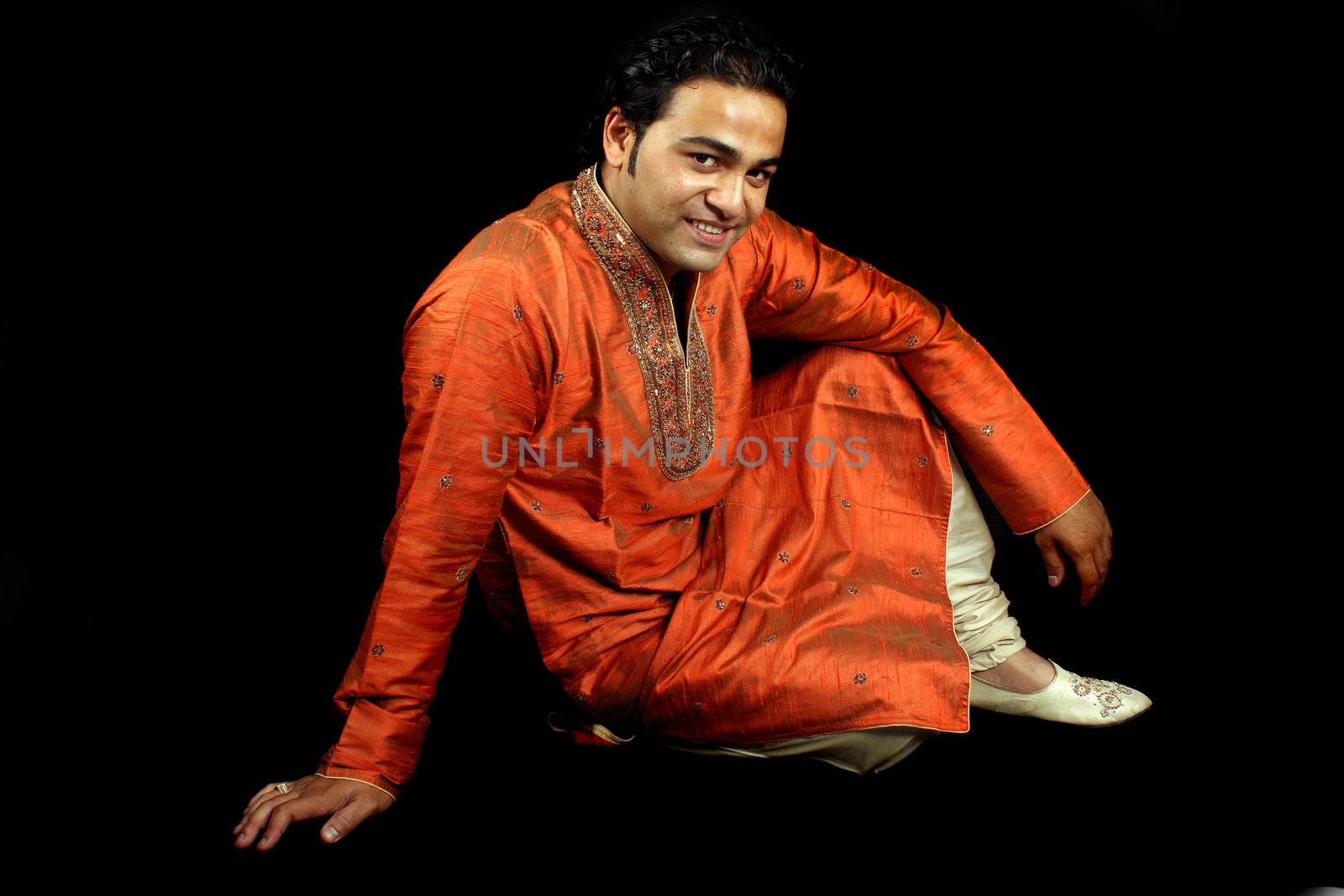 A handsome Indian man in a traditional attire (Shrewani), on black studio background.