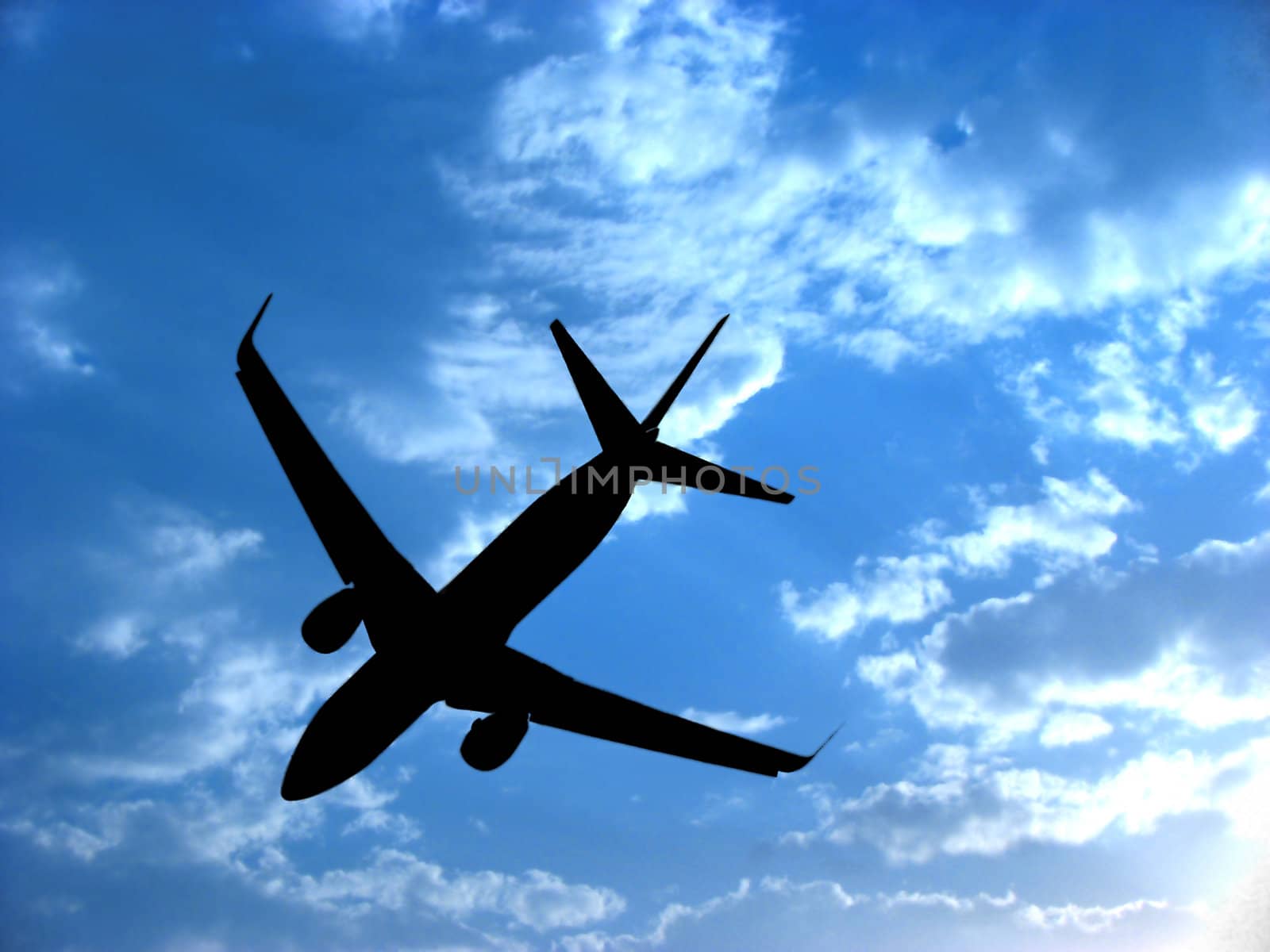 A background with a view of an airplane silhouette against the backdrop of a blue sky with little white clouds.