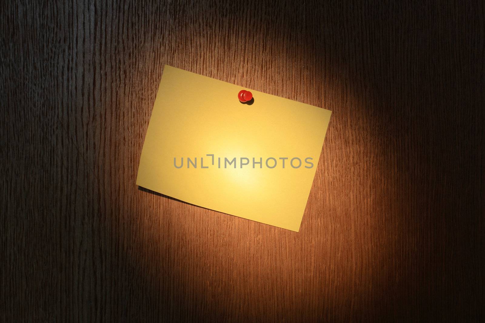 Yellow note pad hanging on dark wooden background under light beam from flashlight