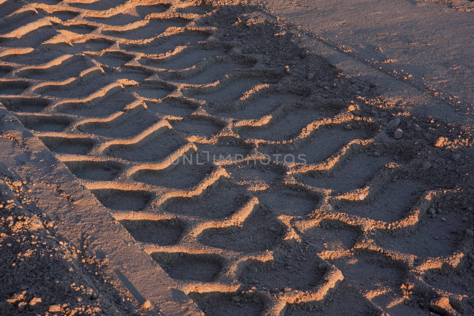 big tire tracks in sand at construction site, sunset light