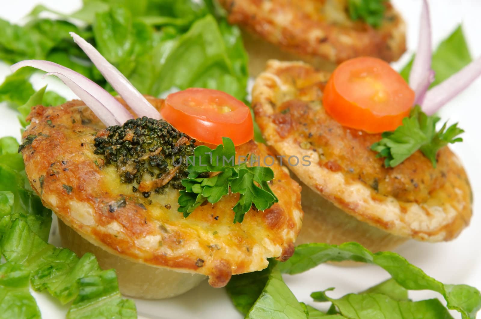 Small vegetable quiche decorated with onion, broccoli, tomato slice and parsley