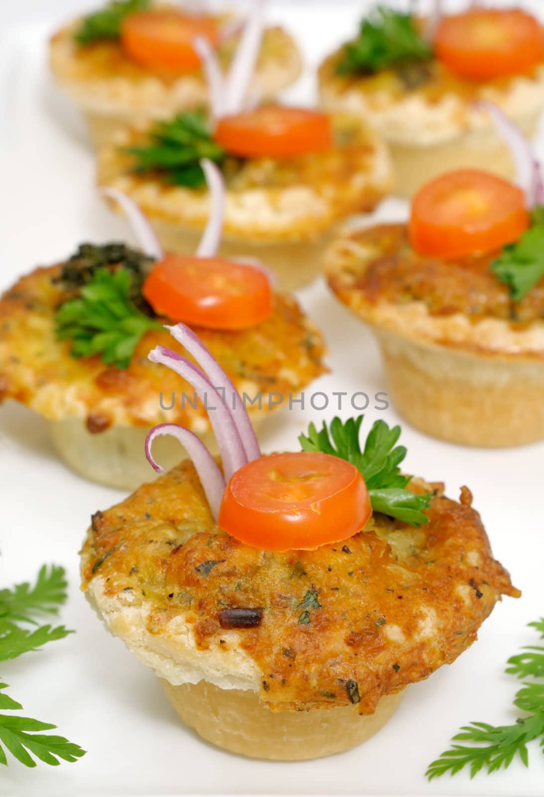 Several vegetable small quiches decorated with onion, tomato slice and parsley
