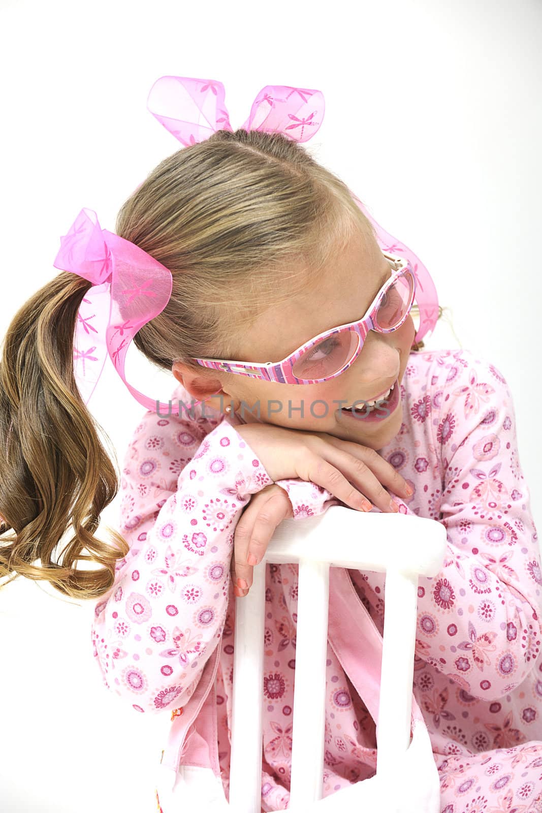 young pretty blond girl with pink sun glasses sitting on a white chair and smiling