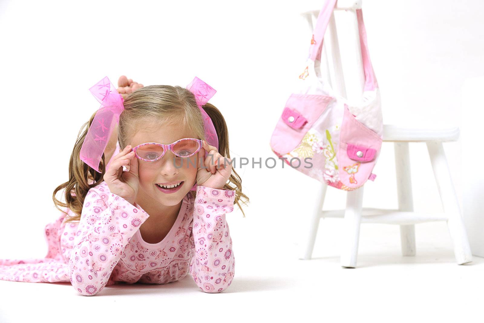 young pretty blond girl with sunglasses, laying on the floor next to a white chair and pink hand bag