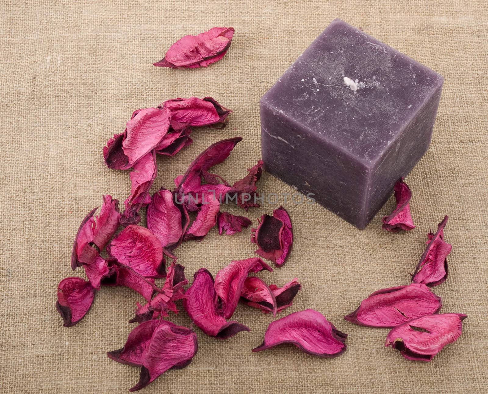 Aromatic purple candle with pink potpourri on linen background