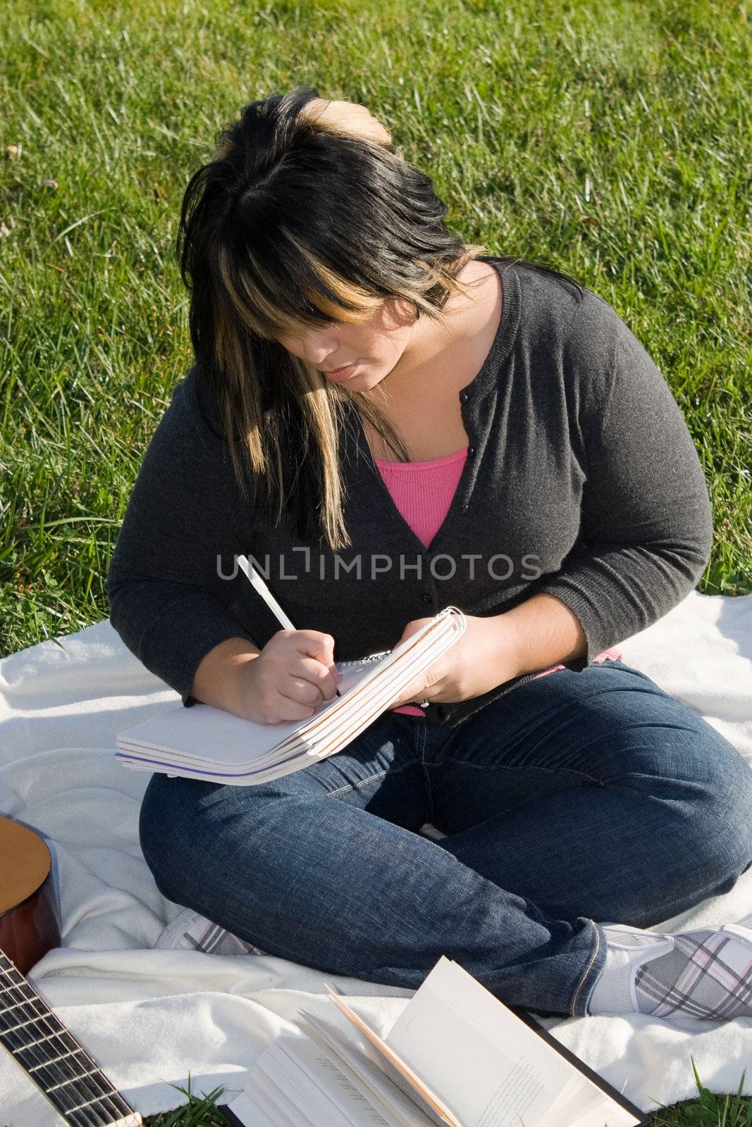 A young musician writing in her notebook while sitting in the grass on a nice day.