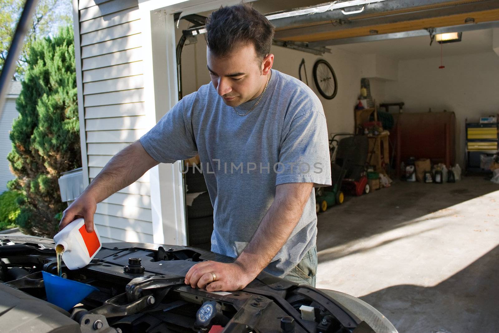 A young man adding oil to his cars engine at the end of an oil change.