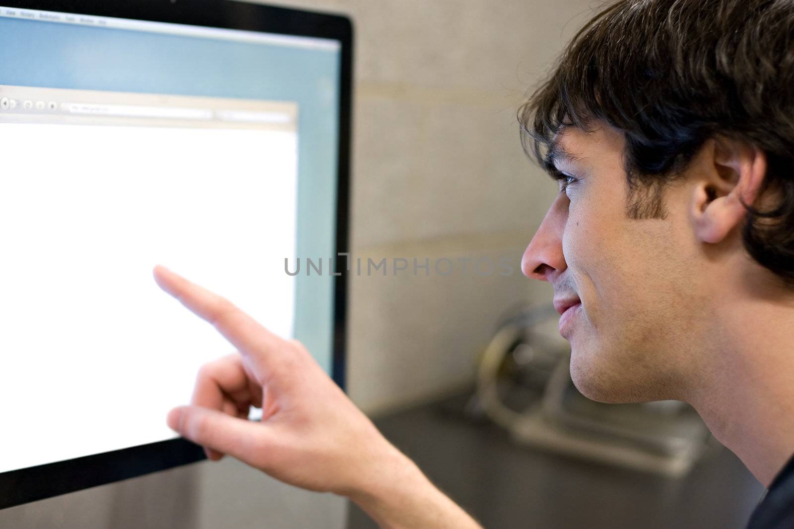 A young man pointing at a modern computer monitor lcd with copyspace.  Shallow depth of field with strongest focus on the face.