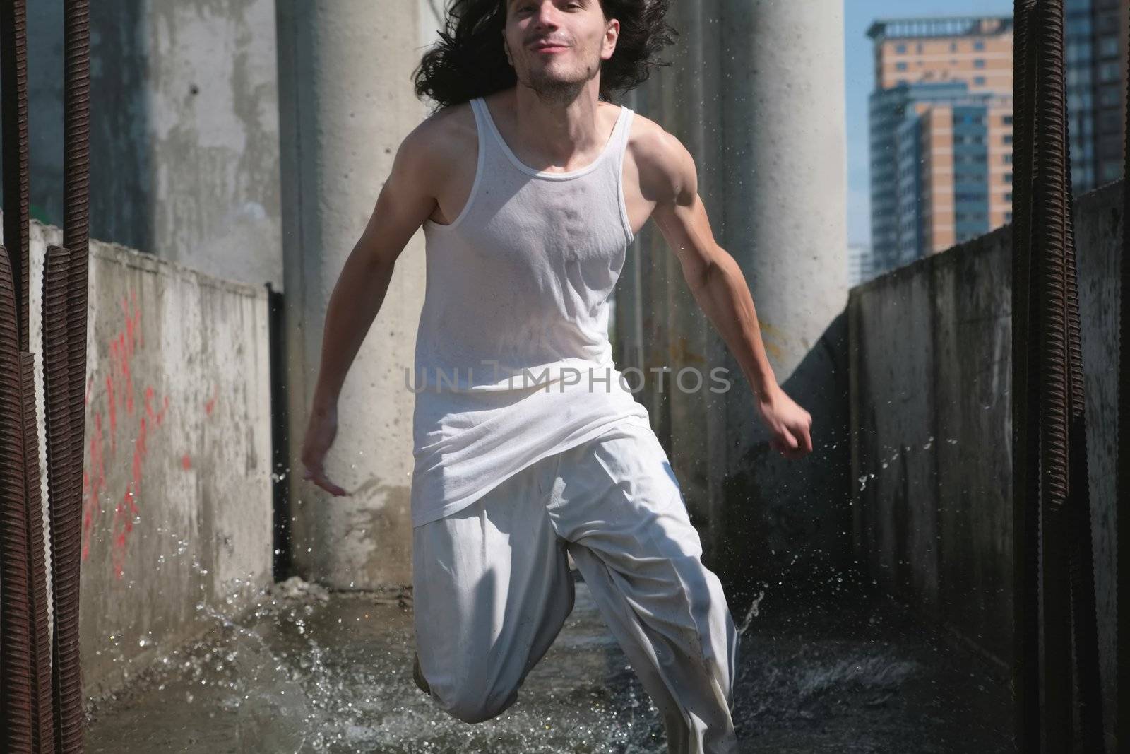 man in white cloth runs on water amongst concrete construction