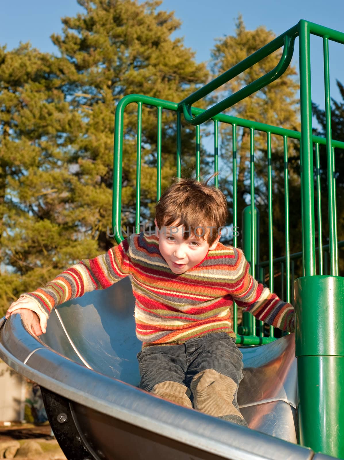 Boy in sweater coming down playground slide by rongreer