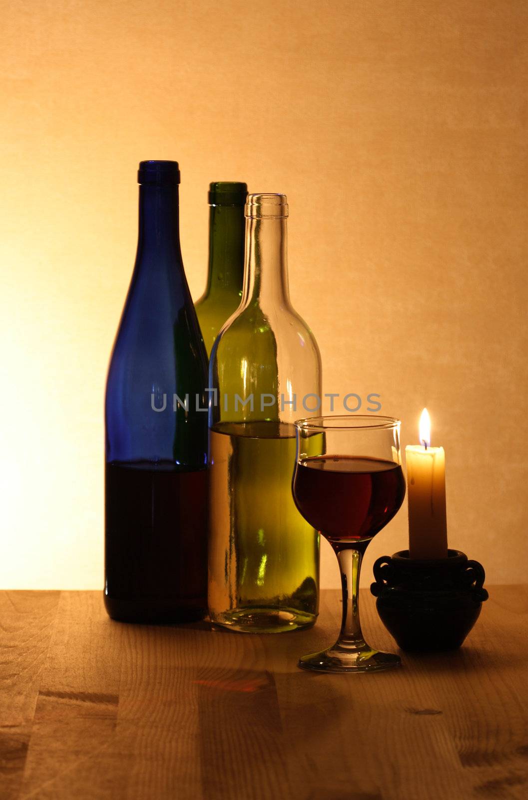 Three bottles of red and white wine wineglass candle on wooden background