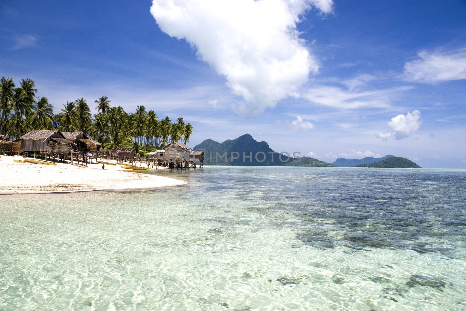 Image of a remote Malaysian tropical island with deep blue skies, crystal clear waters, atap huts and coconut trees.