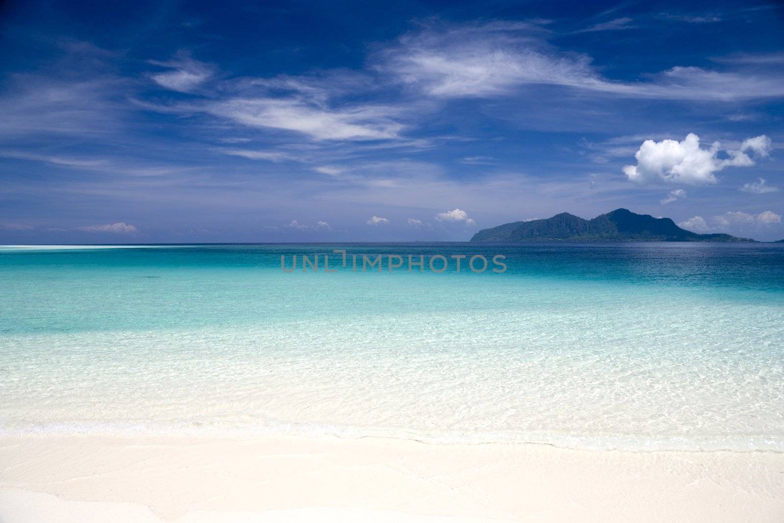 Image of a remote Malaysian tropical island beach with deep blue skies, crystal clear waters and an island in the background.