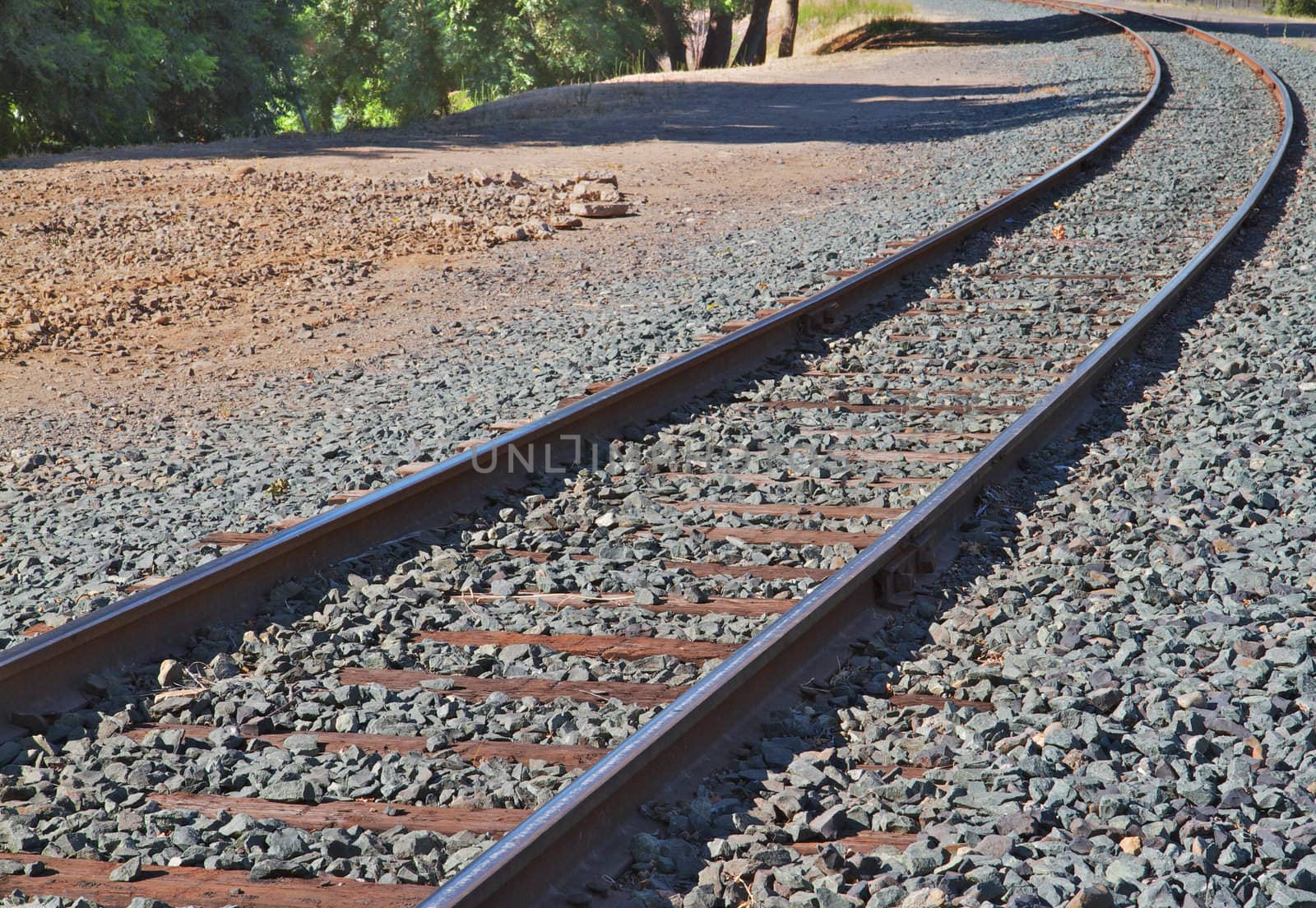 Brightly lit railroad track curve with gray gravel on either side