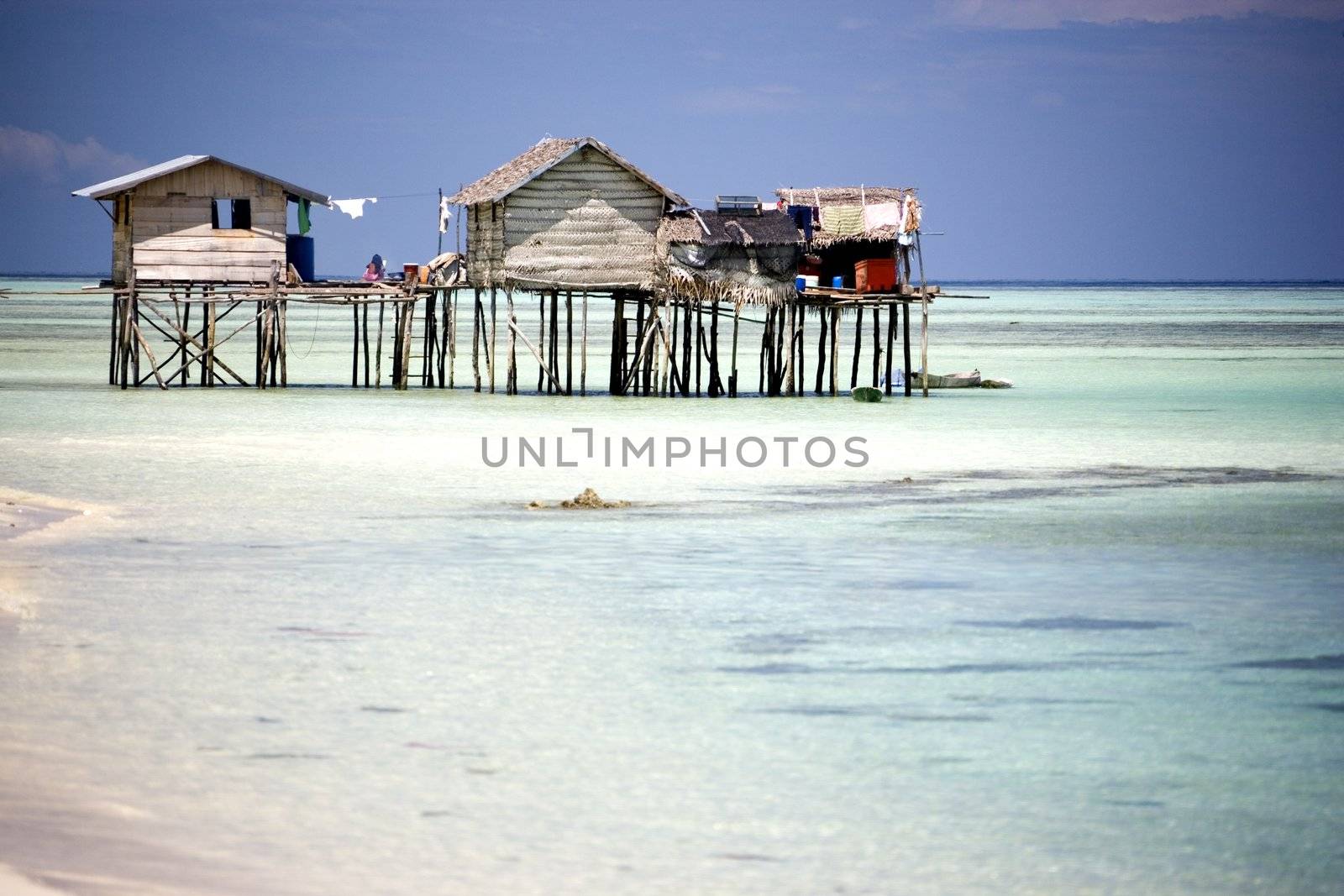 Image of huts on stilts with clear water in the foreground and blue skies in the background.