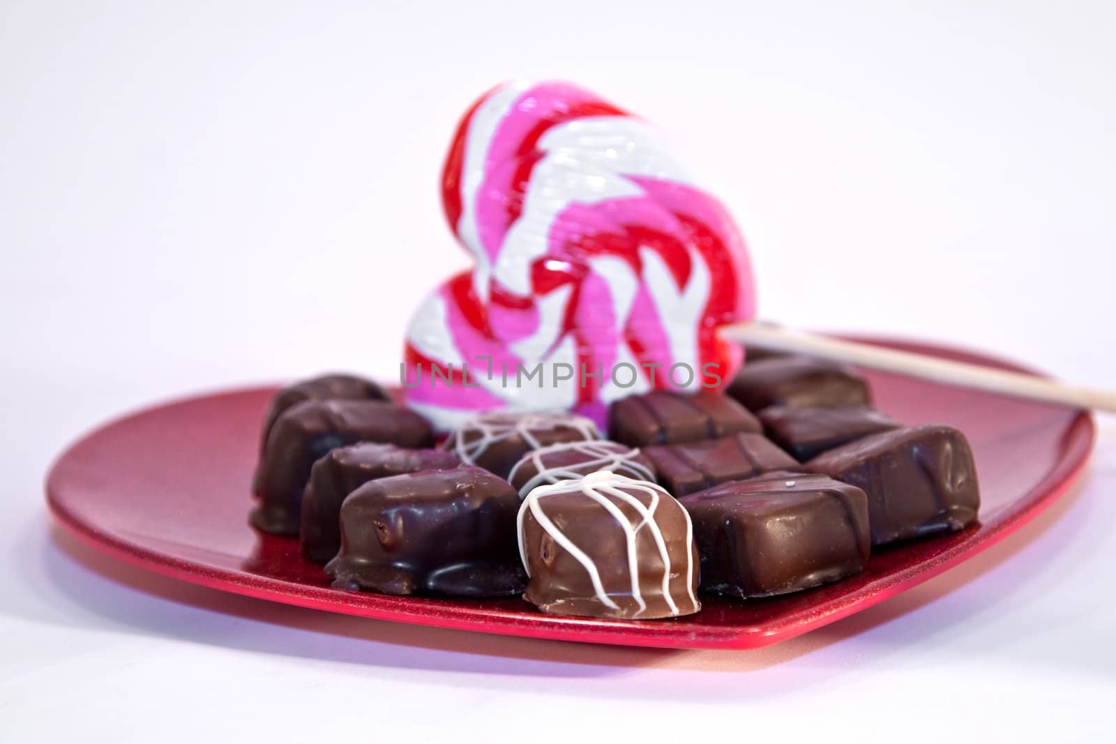 A variety of chocolates with a heart shaped lollipop on a red metallic heart plate isolated on white