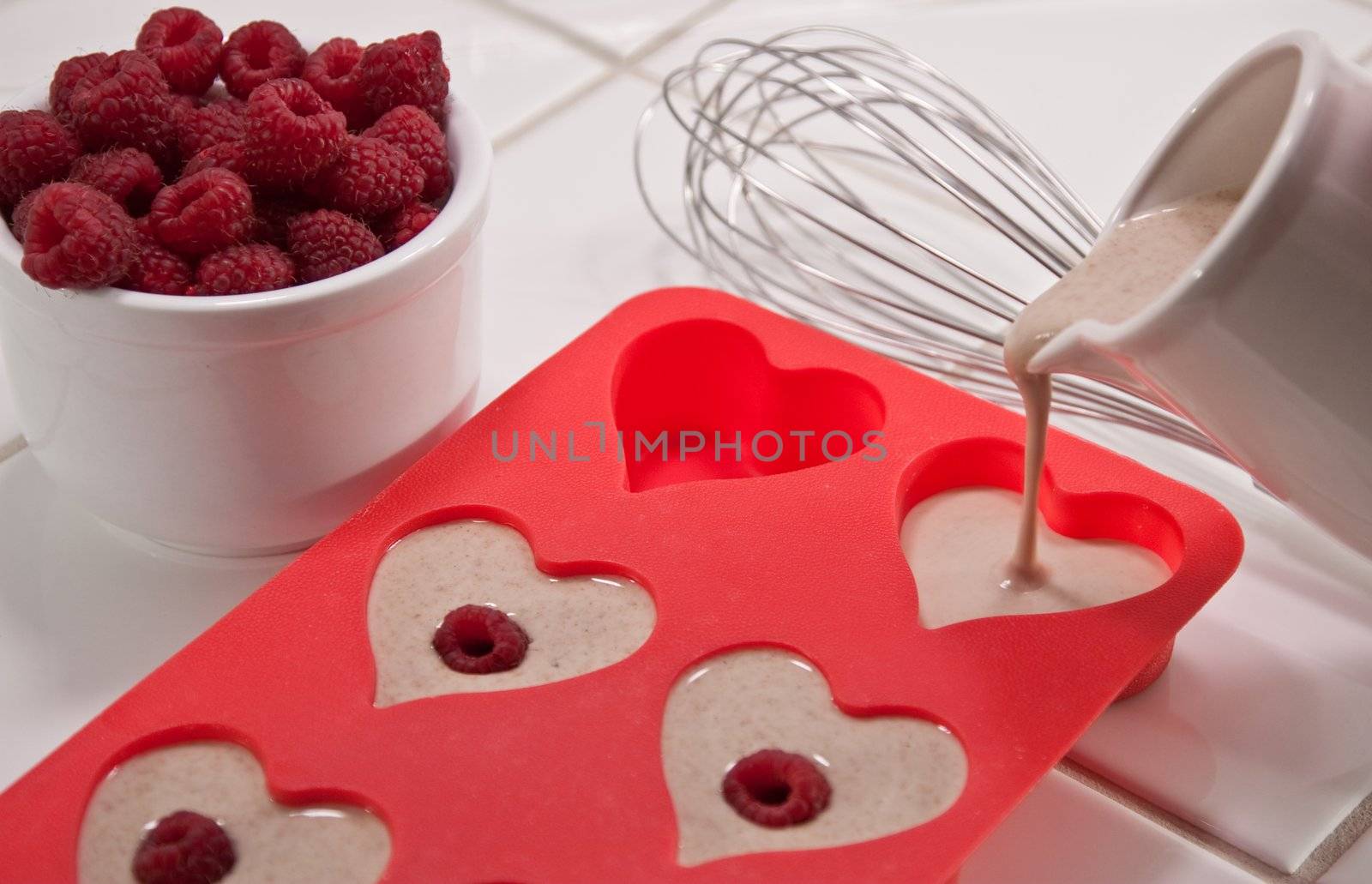 Whisk, bowl of raspberries and heart shaped muffin pan with pouring batter pitcher