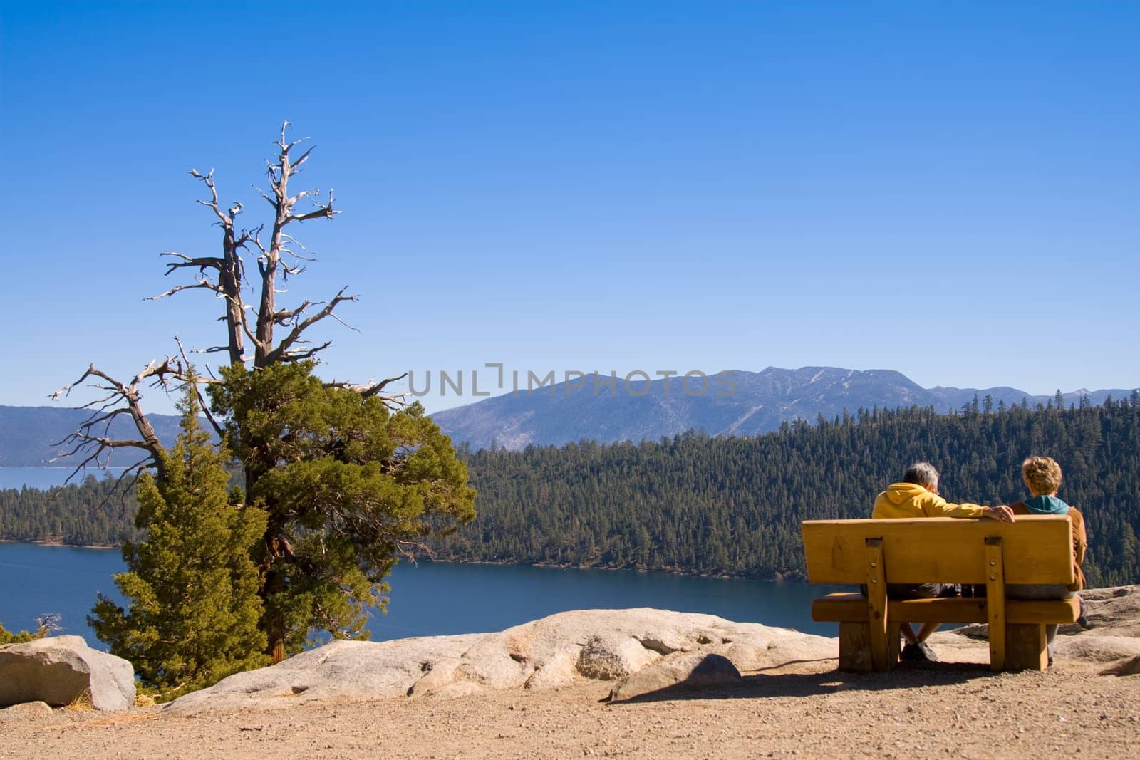 A couple relaxing on bench overlooking a view of mountain lake