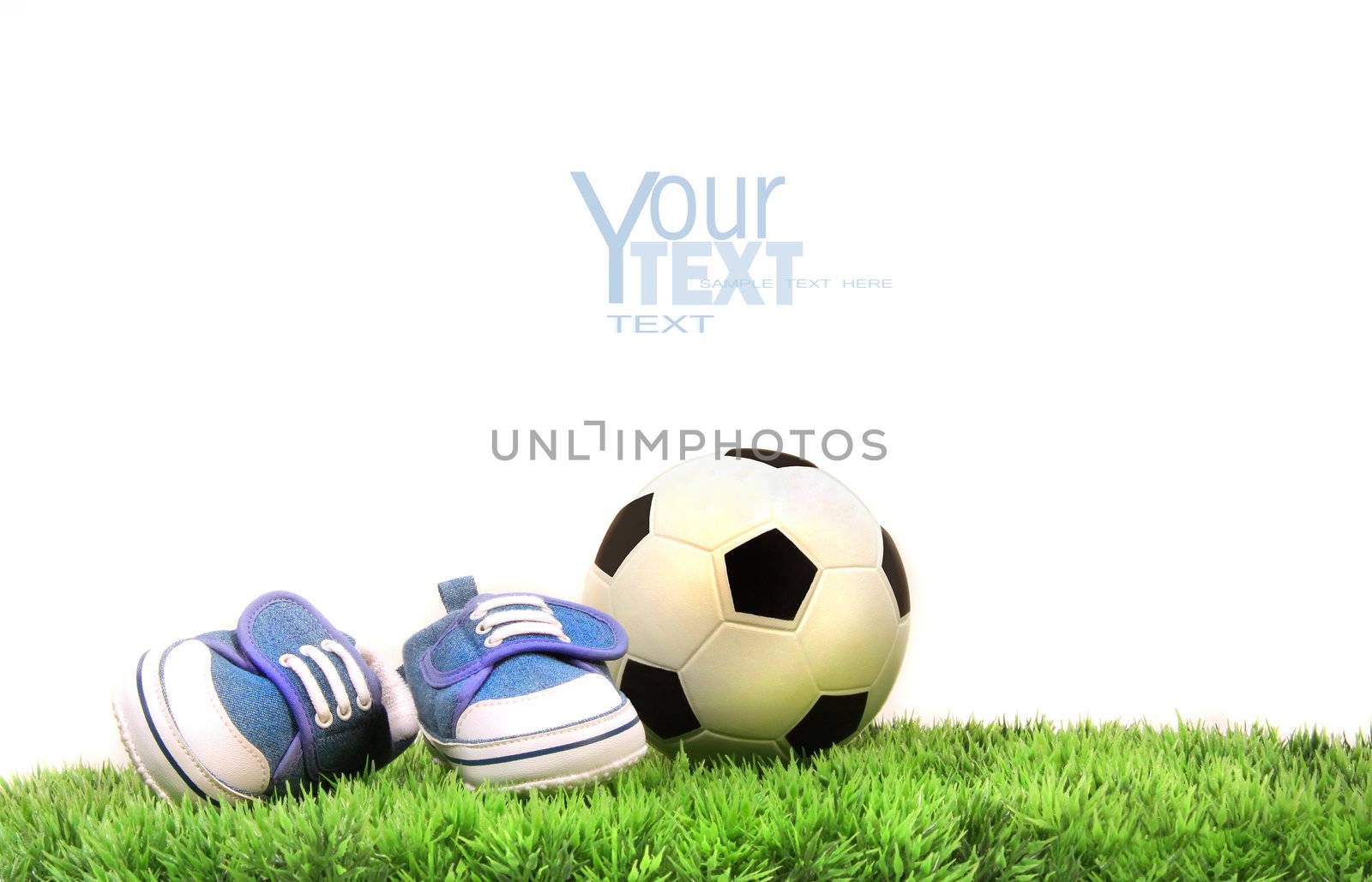 Child's shoes with rubber ball on grass against white background