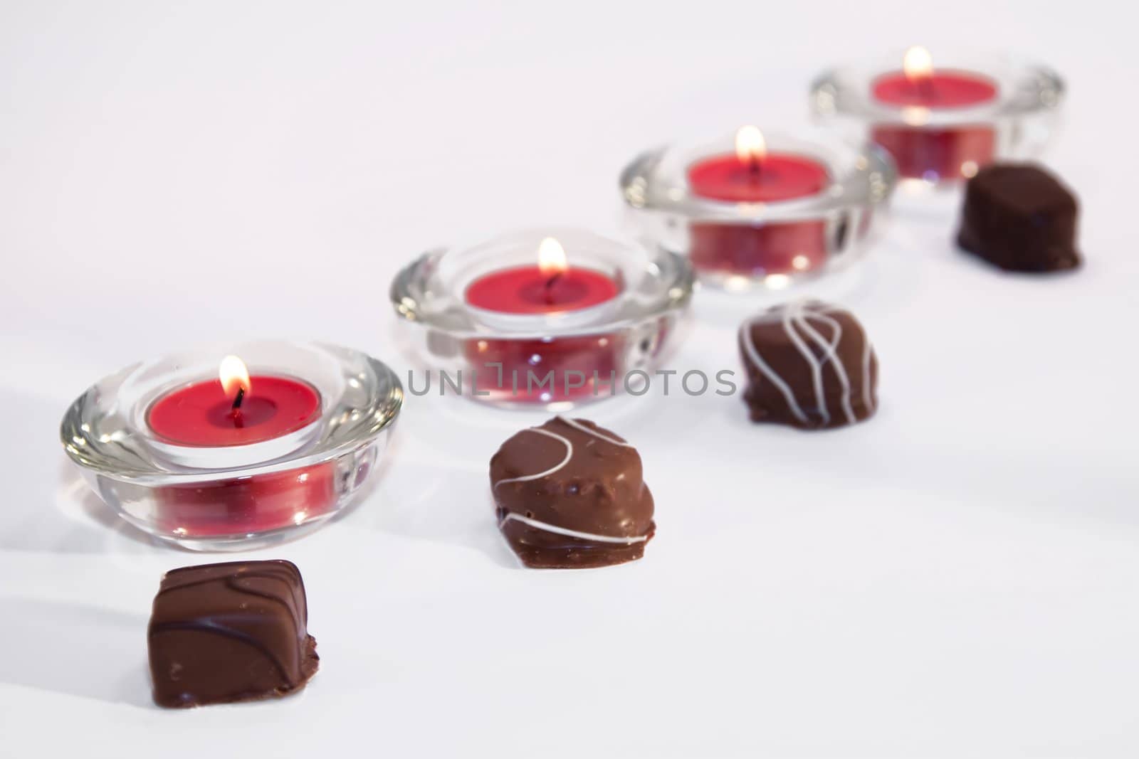 Line of red lit candles with chocolates on white background