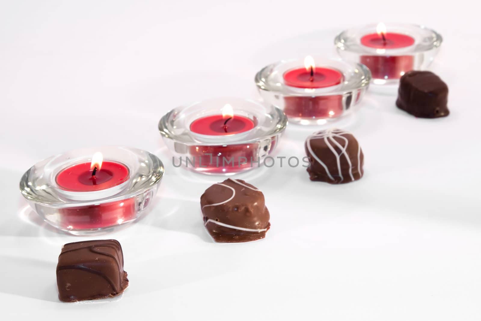 Line of red lit candles with chocolates on white background