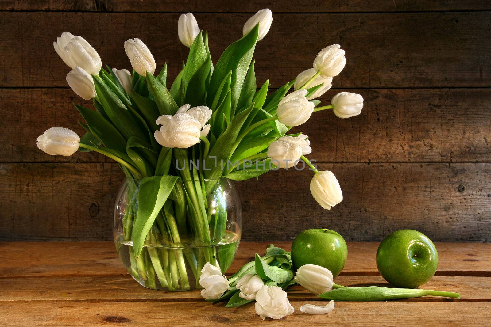 White tulips in glass vase with rustic wood background