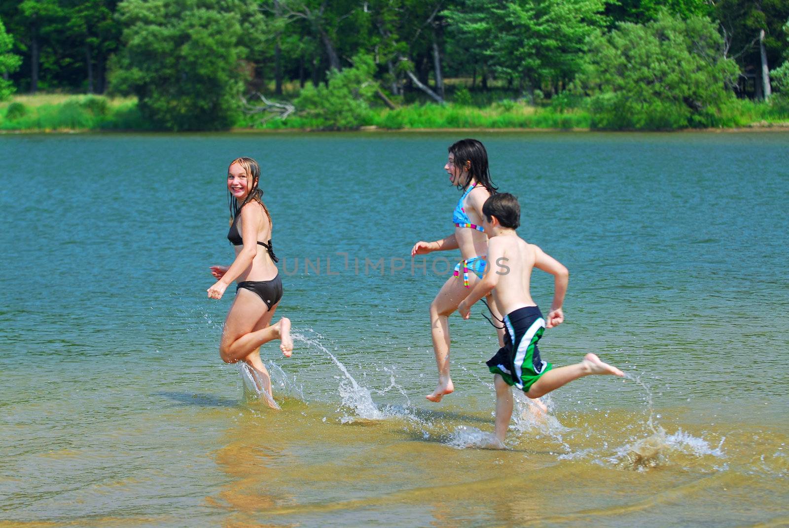Group of children running into clear lake water