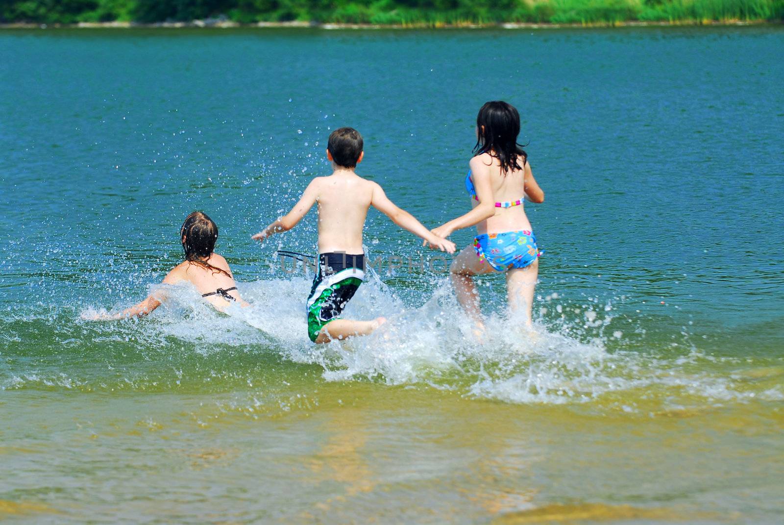 Group of children running into clear lake water