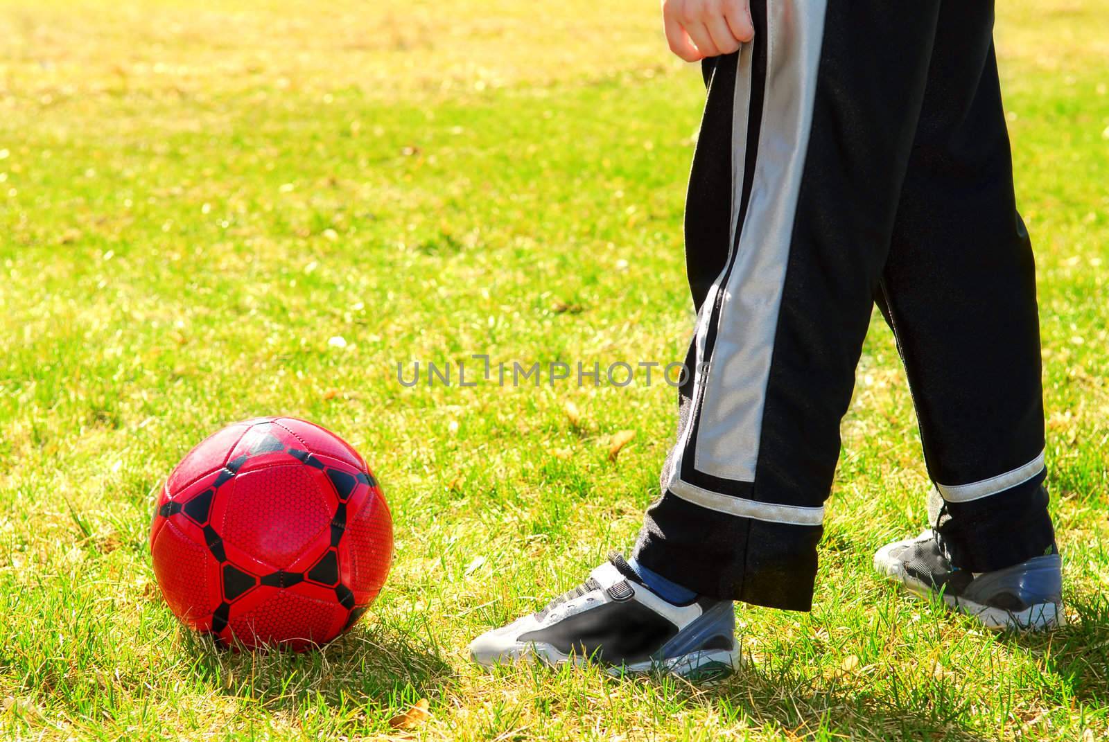 Young boy playing with red soccer boy outside