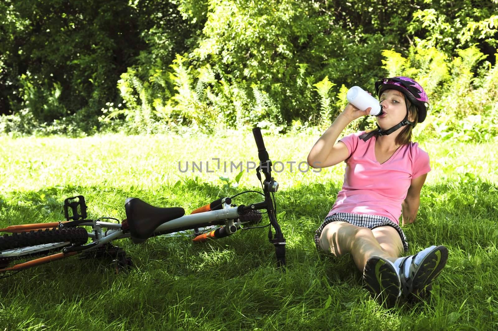 Teenage girl resting in a park with a bicycle drinking water