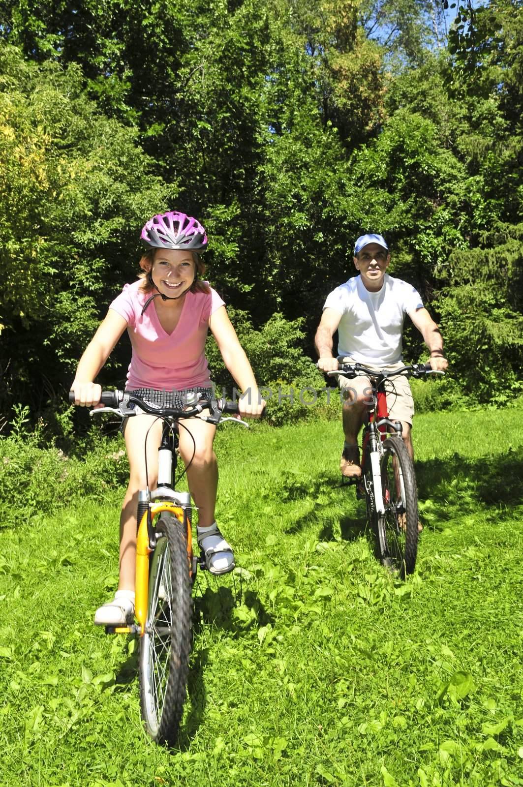 Teenage girl and her father riding bicycles in summer park