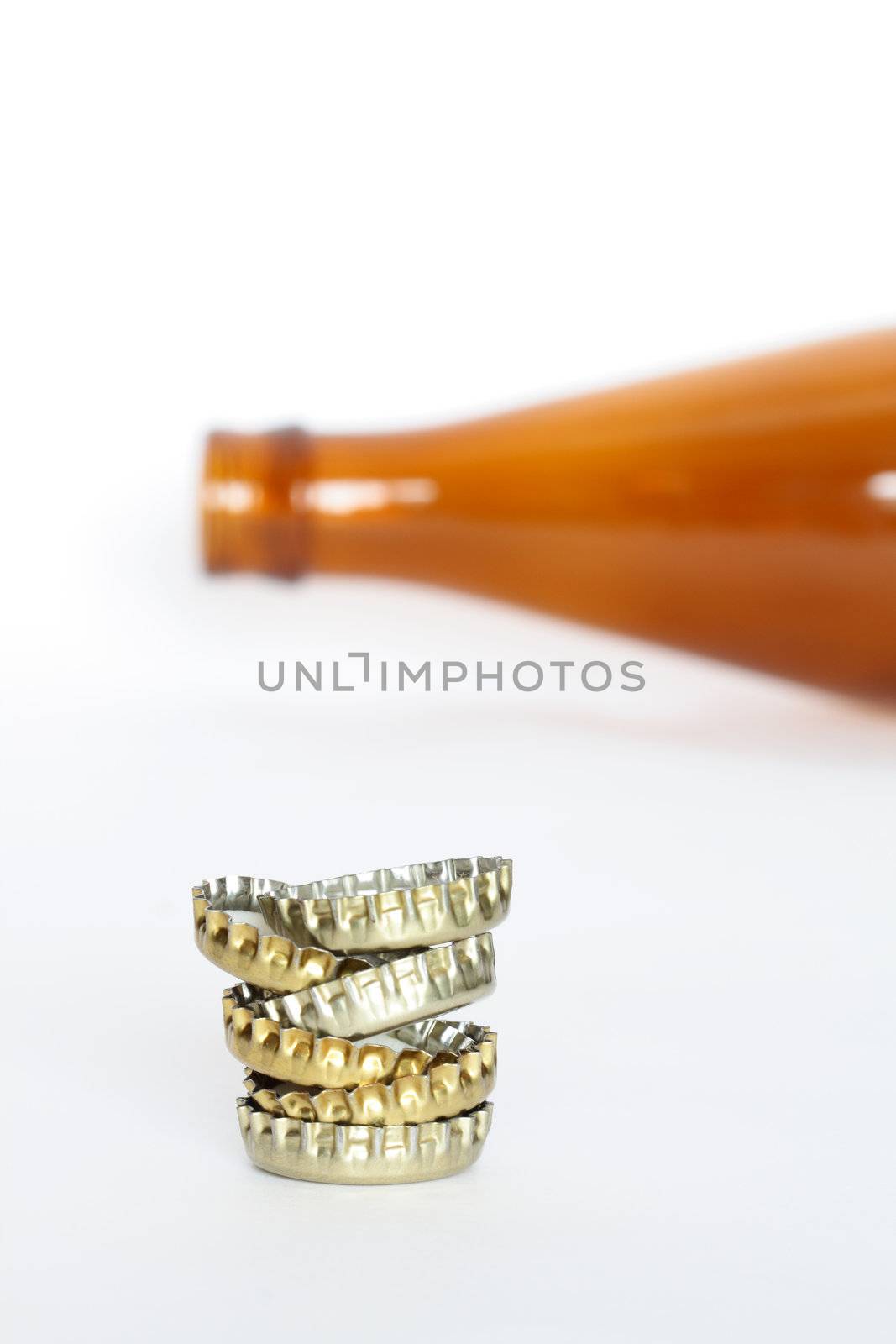 Stack of bottle caps on white background with lying empty bottle